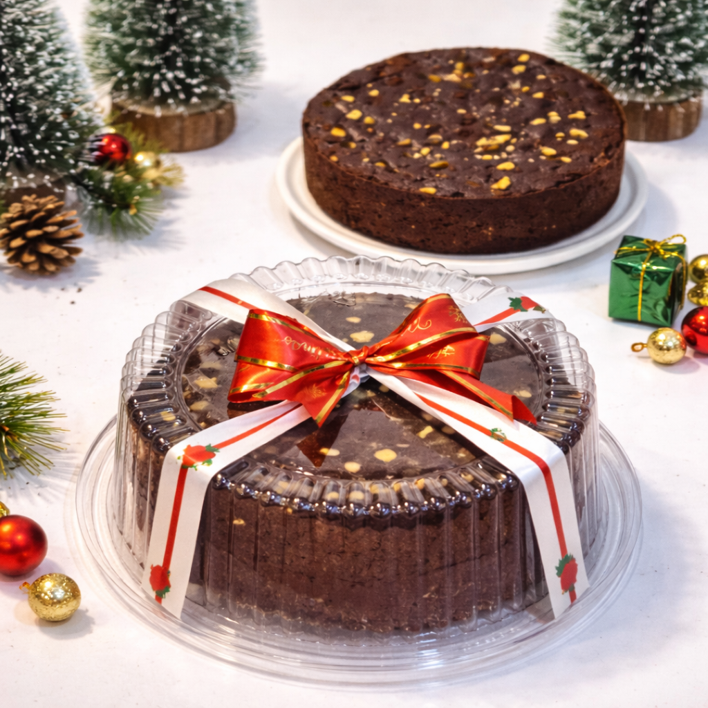 Chocolate cake wrapped in clear plastic with a red ribbon, surrounded by Christmas decorations.